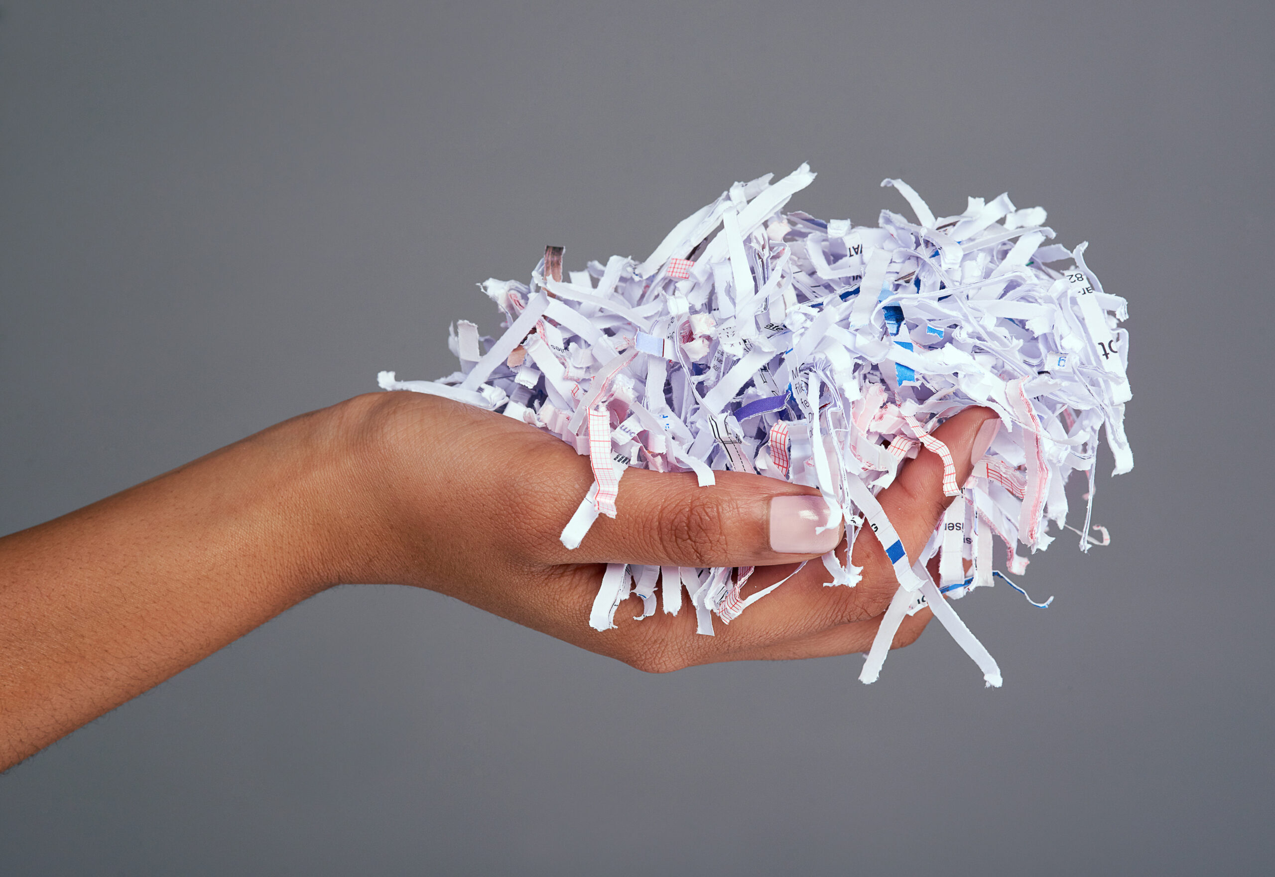 Studio shot of a womans hand holding a pile of shredded paper against a grey background.