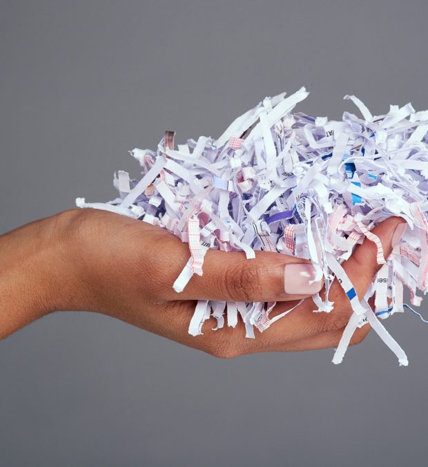 Studio shot of a womans hand holding a pile of shredded paper against a grey background.
